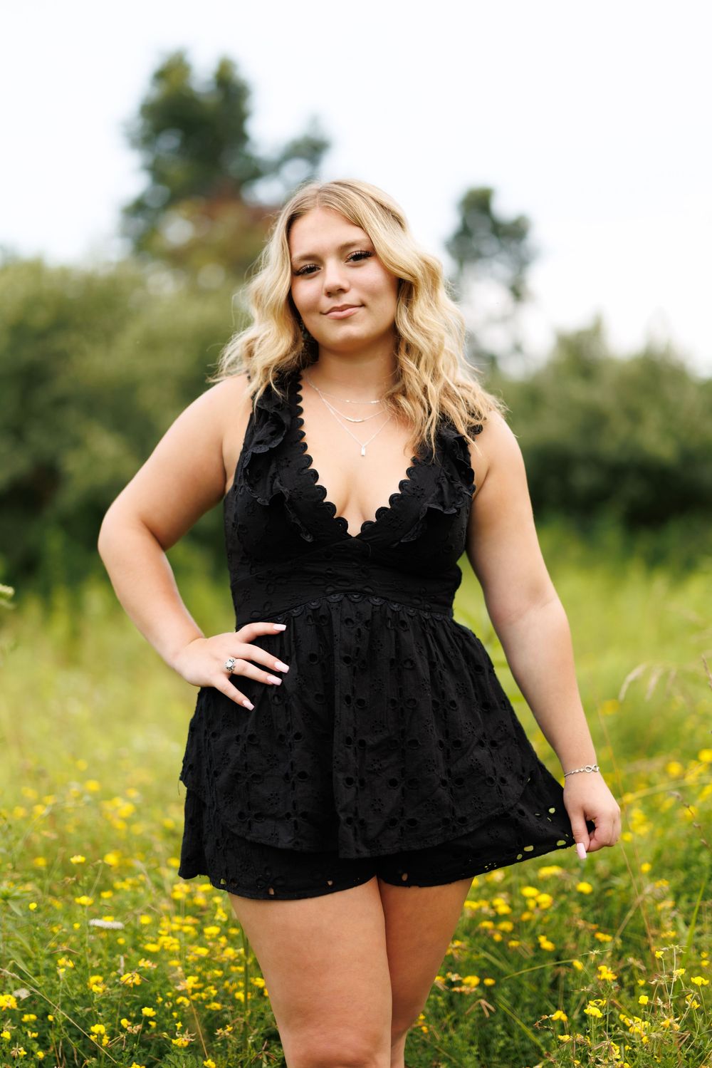 Woman wearing black lace romper poses confidently in a sunny wildflower field.
