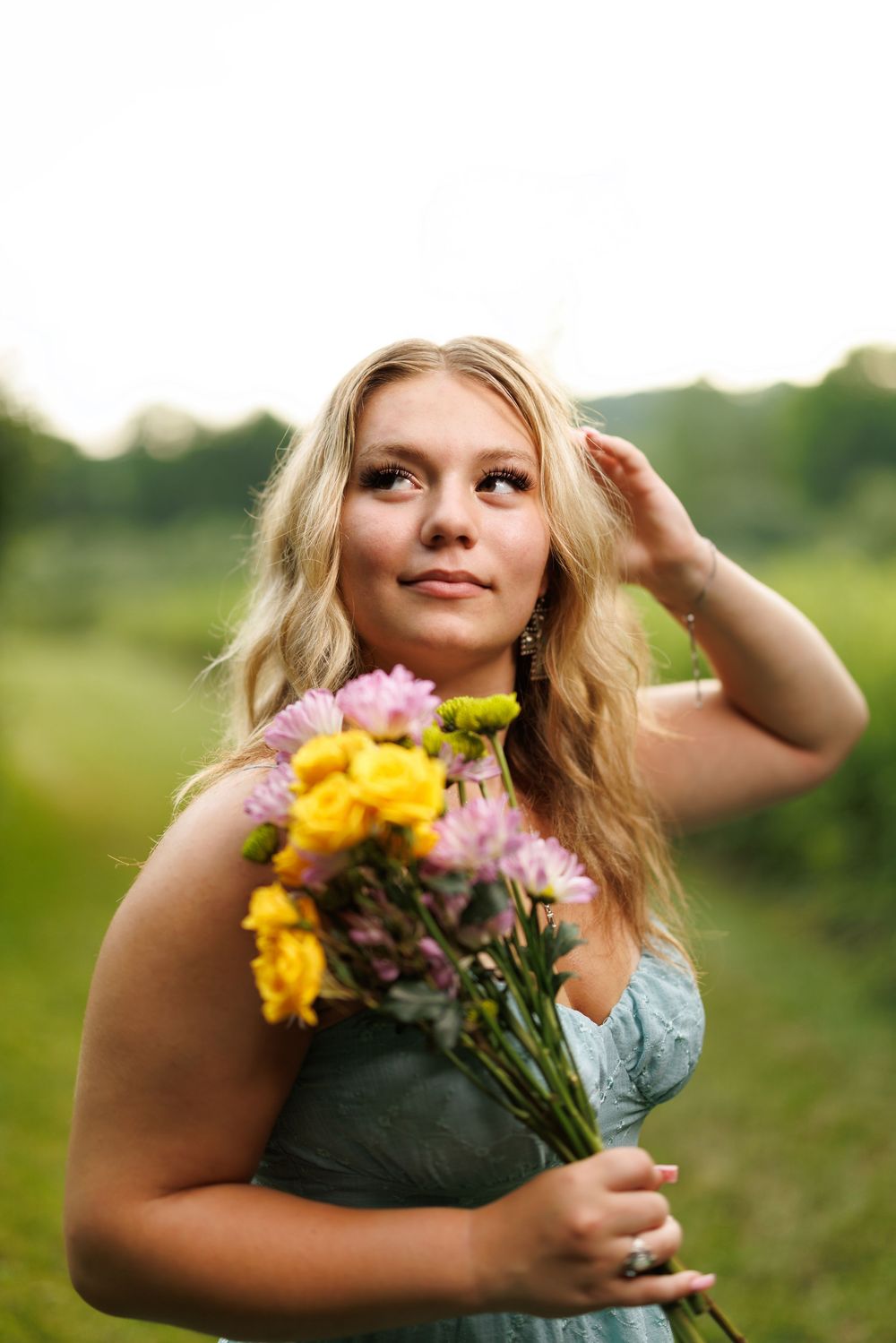 Person holding colorful summer flowers while posing in outdoor natural setting.