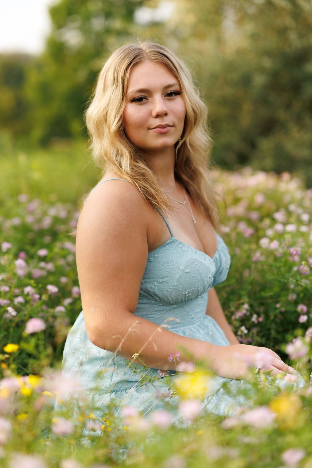 Person in pale blue dress sitting among blooming wildflowers in natural setting.