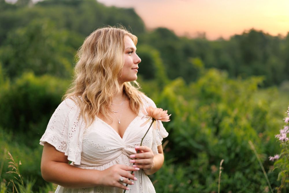 A white lace top and denim outfit photographed in a lush green outdoor setting during golden hour.