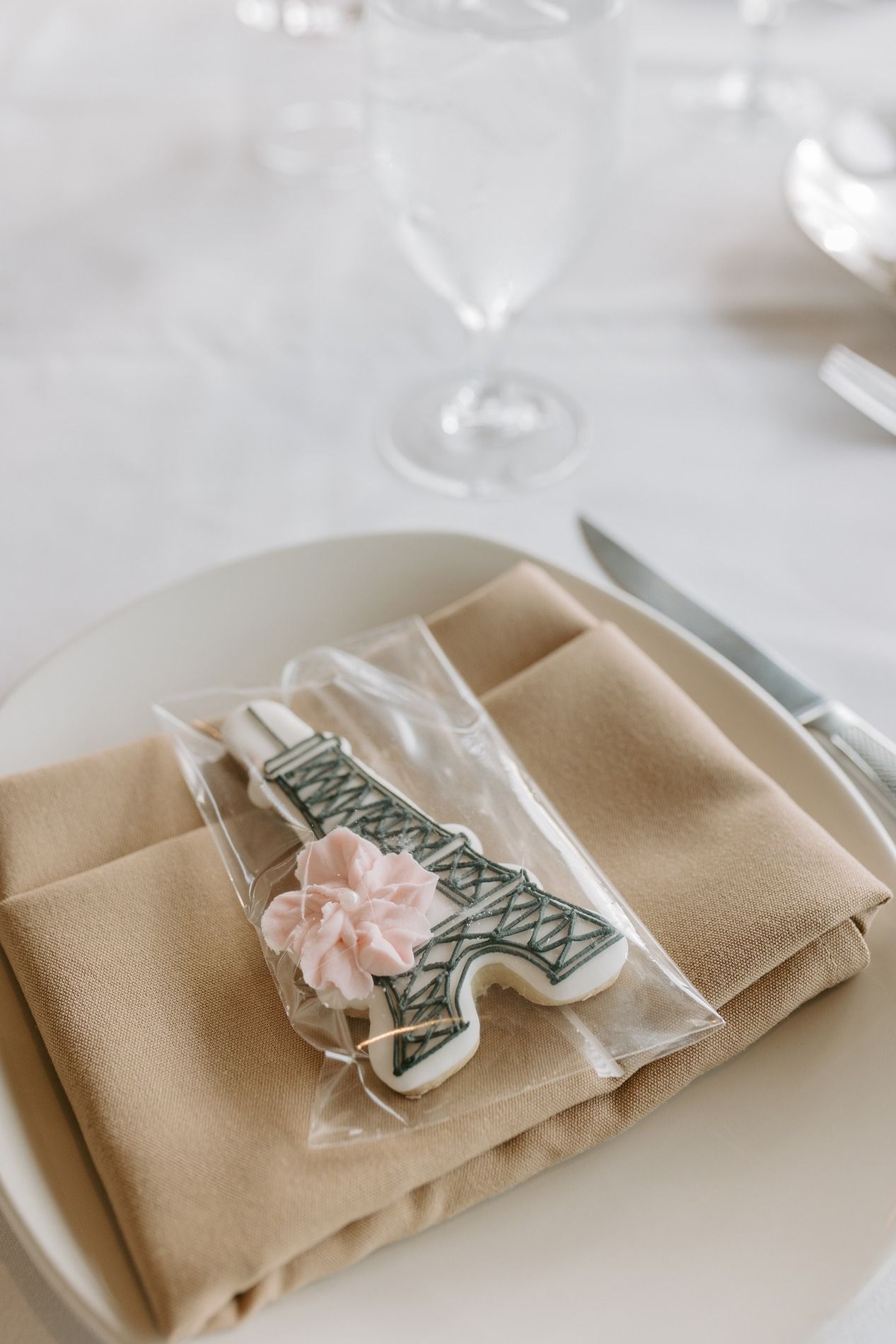 Elegant place setting with beige napkin and Eiffel Tower cookie on white plate at a Valentine's Day themed wedding.