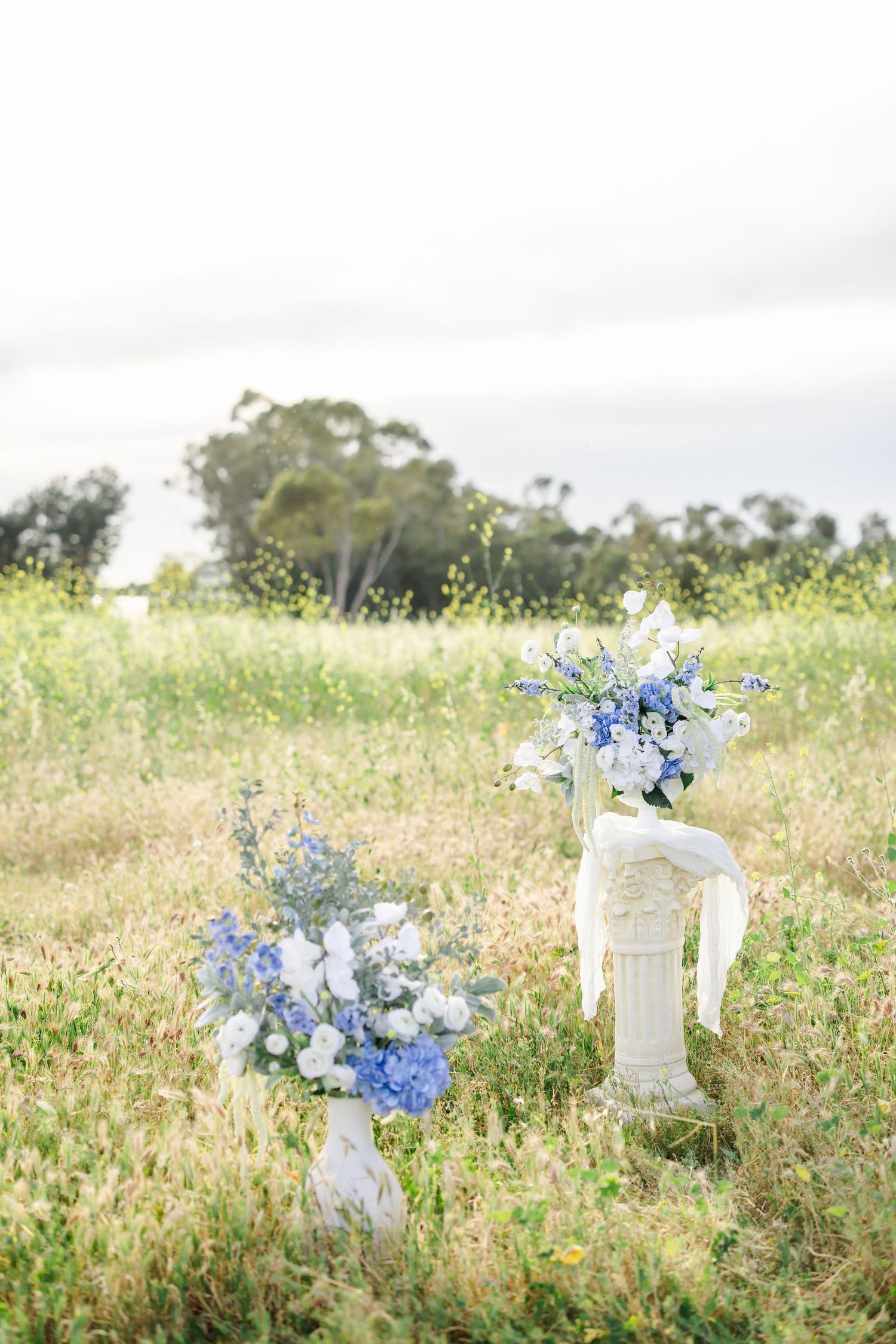 White and blue floral arrangements displayed in an outdoor field setting with decorative pillars.