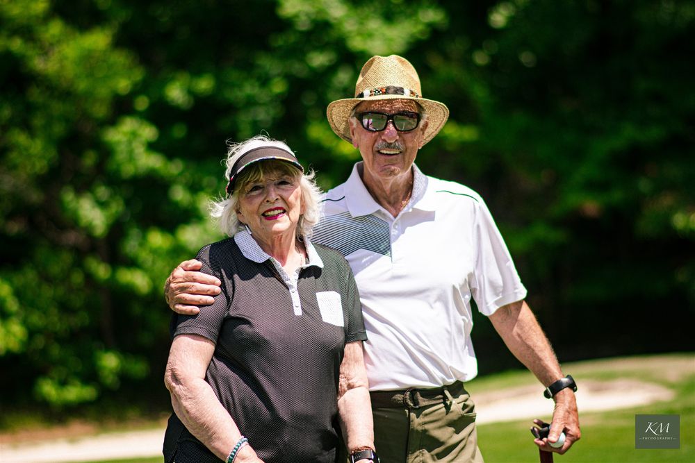 A man and a women smiling outside with golf clubs, Birmingham Alabama corporate event photographer.