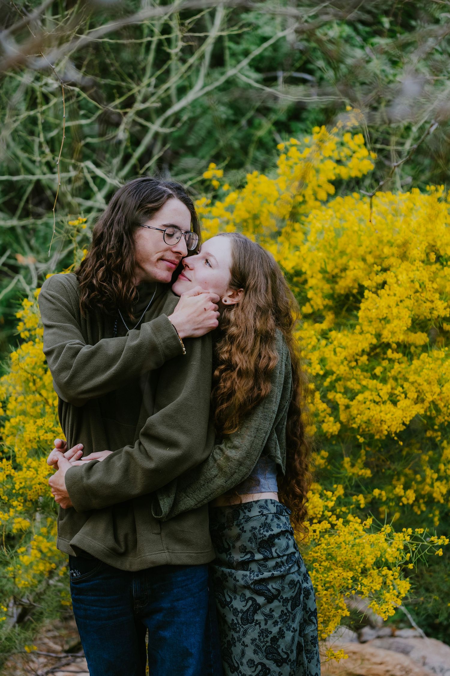 Romantic couple sharing affectionate moments against vibrant yellow flowering bushes.