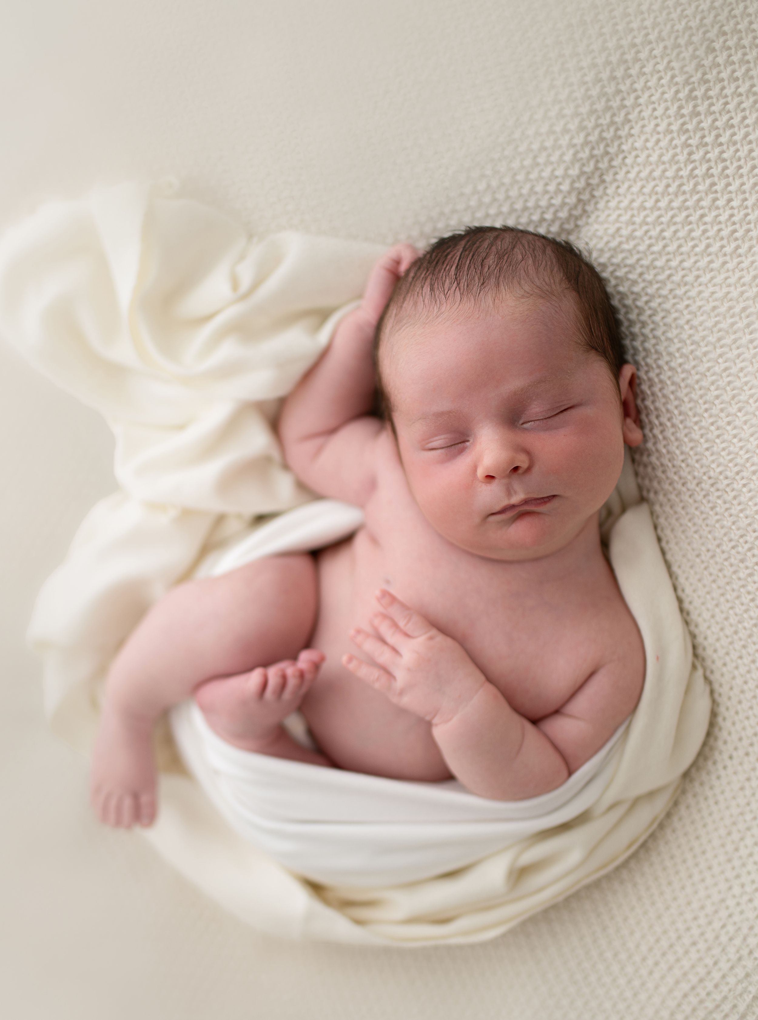 Peaceful newborn baby sleeping wrapped in a soft cream blanket during a professional newborn photography session.