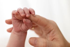 A newborn baby grasping an adult's finger, symbolizing the bond between parent and child.