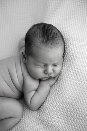 Black and white photo of a peaceful sleeping newborn baby curled up on a soft knit blanket.