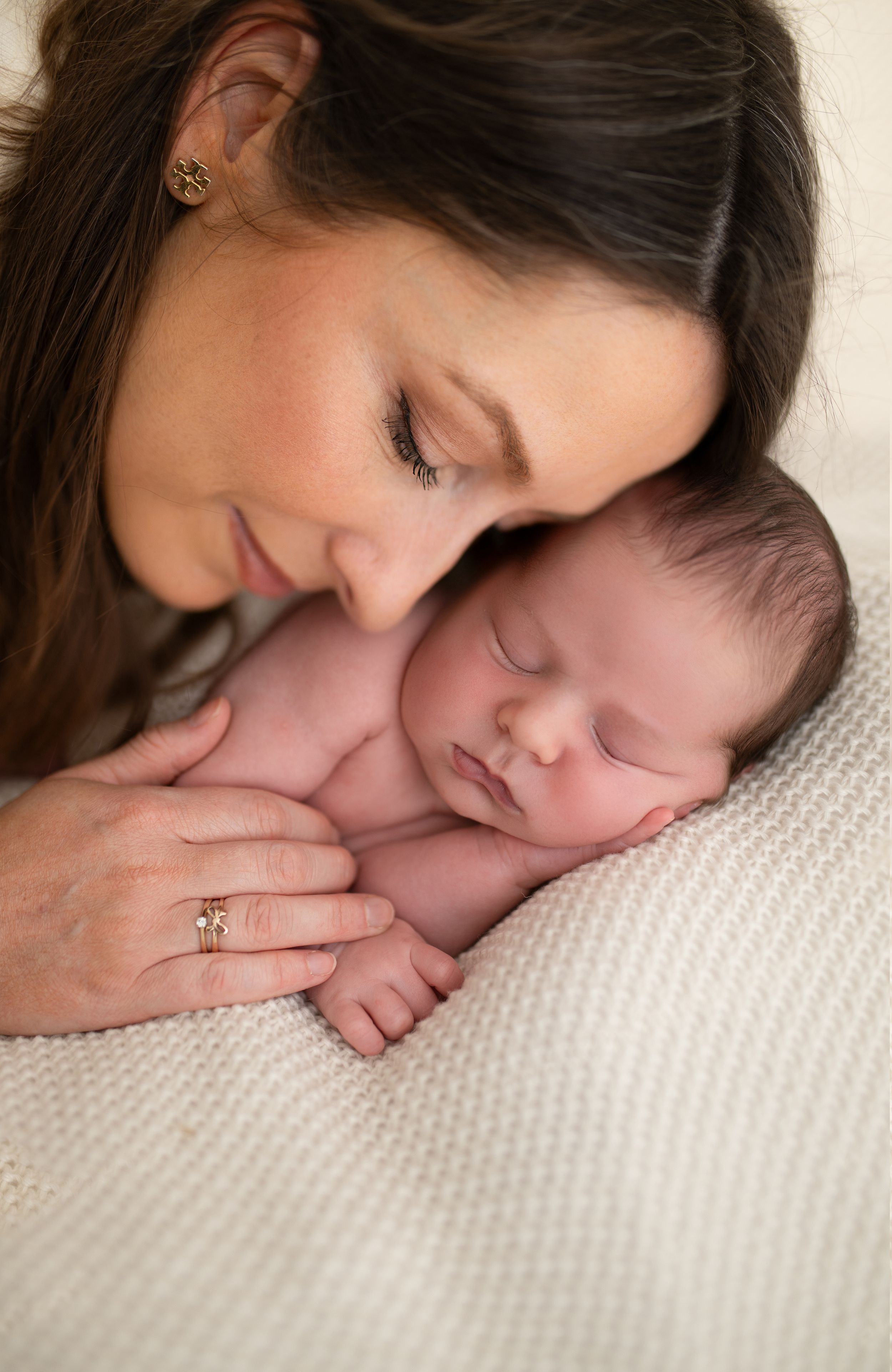 A mother tenderly gazes at her sleeping newborn baby resting on a soft white blanket in a serene portrait.