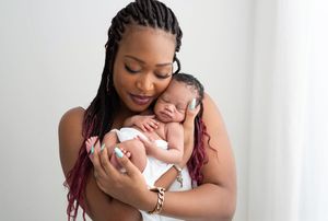 A tender moment between mother and sleeping newborn baby against a white background.