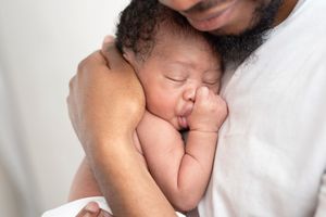 A newborn baby sleeps peacefully while wrapped in soft white blankets during a professional photo session.