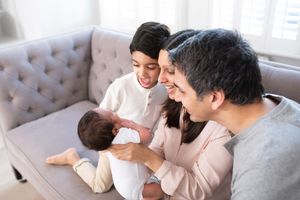 A family shares a tender moment together while sitting on a gray tufted couch in a bright living room.