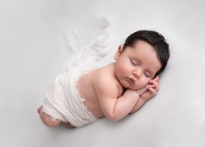 A sleeping newborn baby in white lace clothing lies peacefully on a soft white backdrop in a series of photos.