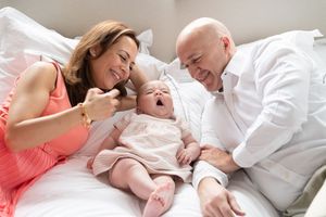Parents share tender moments with their newborn baby while lying together on white bedding.
