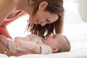A tender moment between parent and baby as they share loving kisses and snuggles on a white bed.