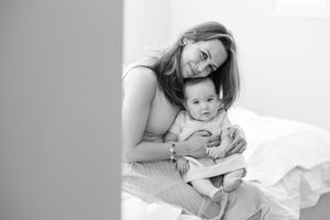 A tender black and white portrait of a parent and baby snuggling together on white bedding.