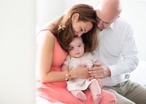 A family in soft neutral colors cuddles together on a white bed during a lifestyle photo session.