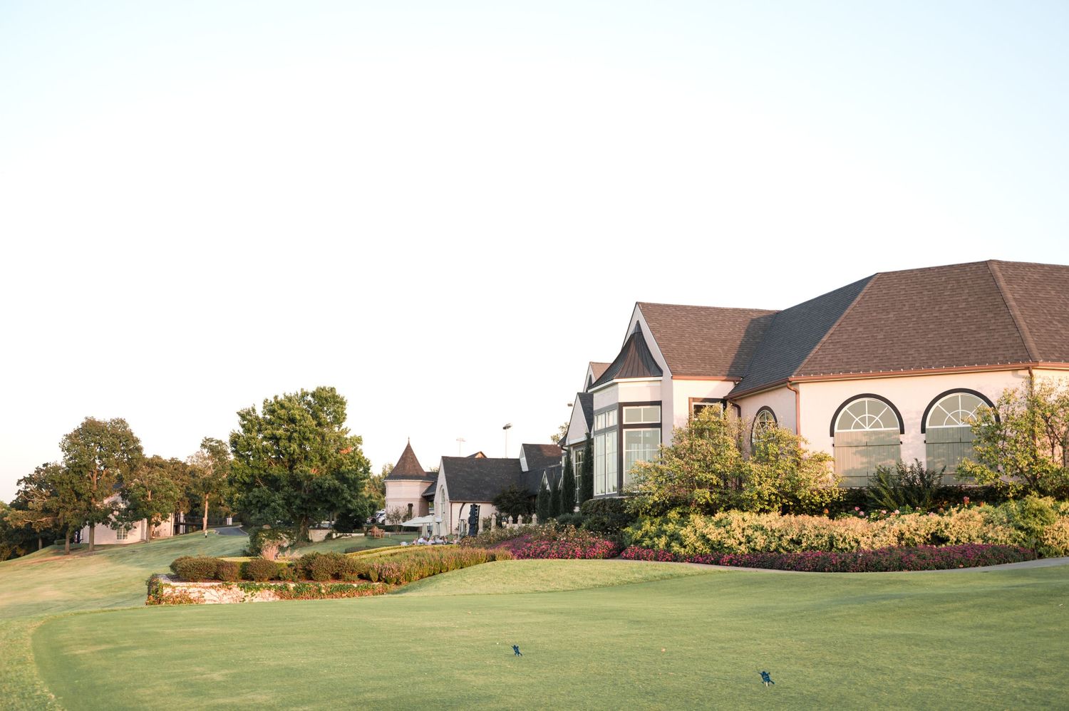 Panoramic view of a golf course clubhouse with lush green fairways and landscaped gardens in the foreground.