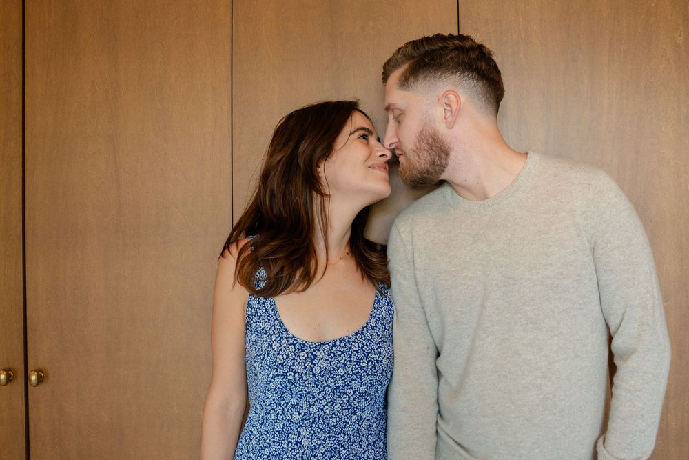 A couple in casual wear share an intimate moment against a wooden wall background.