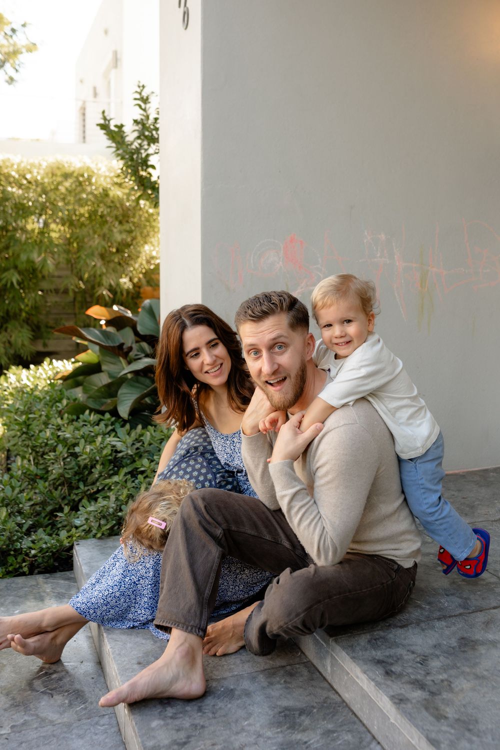 A family sits together on outdoor steps during golden hour, sharing playful moments in a garden setting.