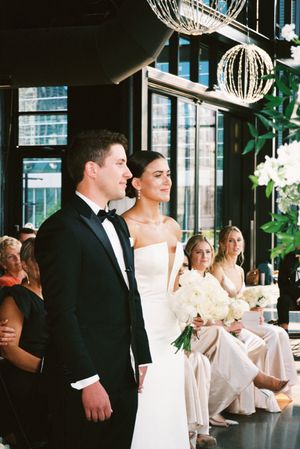 A wedding couple and guests celebrate at an elegant indoor reception with crystal chandeliers and greenery decor.