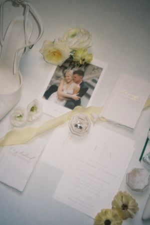 Wedding stationery layout with white invitations, delicate yellow flowers, and a photograph displayed with elegant shoes.