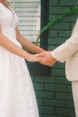 Close-up view of hands exchanging a white wedding dress against a green brick wall background.