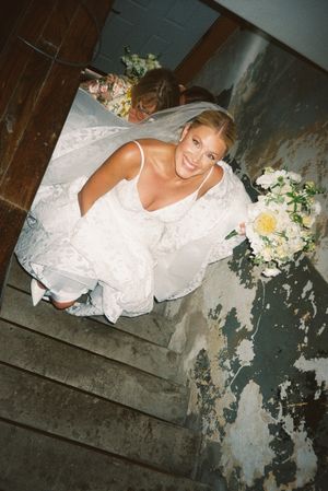 A person in a white wedding dress poses on rustic stairs with floral bouquet decorations.