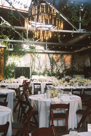 Elegant wedding reception venue with white round tables, string lights, and greenery decorations creating a romantic atmosphere.