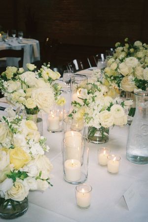 White and cream floral centerpieces with glowing candles arranged on elegant table settings.