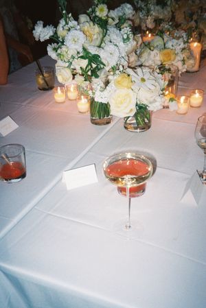 White tablecloth setting with glowing candles and floral centerpieces featuring cocktail glasses.