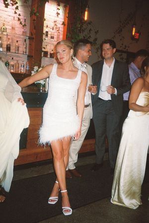 Wedding party guests dancing and mingling at a reception with exposed brick walls and ambient lighting.