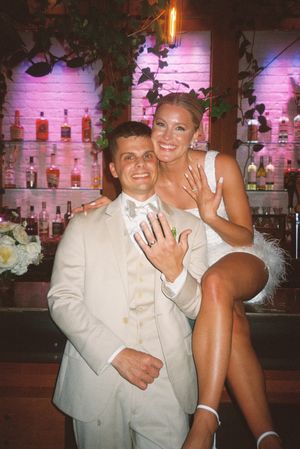 Couple in a dimly lit bar with pink lighting and bottles displayed on shelves in the background.