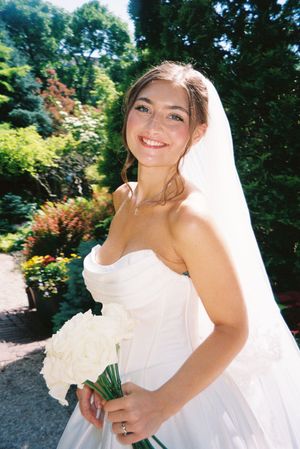 A sunny outdoor garden wedding photoshoot with vibrant greenery and colorful flowers in the background.