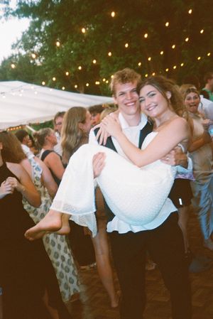Wedding guests dance and celebrate under twinkling lights at an outdoor evening reception.