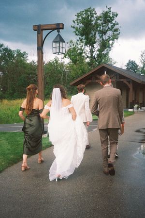 A sequence of wedding party members walking down a paved path in brown and white attire.