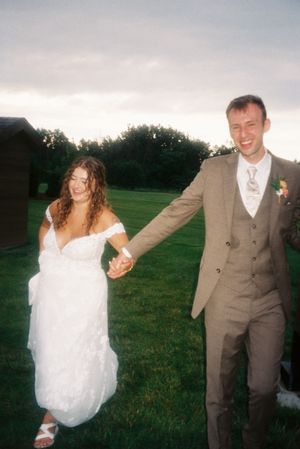 A bride and groom dance playfully in a grassy field at sunset, creating a series of joyful candid moments.