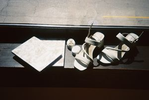 A pair of white ballet shoes sits on a dark surface next to sheet music in a dramatic lighting setup.