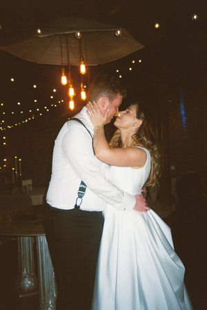 A couple shares their first dance as newlyweds under hanging lights and an umbrella at their evening reception.