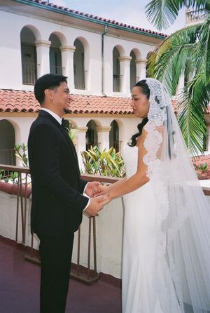 A wedding couple shares an intimate moment in a Spanish-style courtyard with arched columns and palm trees.