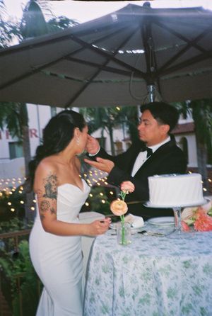Wedding reception scene with guests dining at tables decorated with floral tablecloths under outdoor lighting.