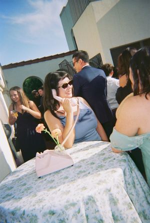 Casual outdoor reception gathering with guests socializing around tables with floral tablecloths.