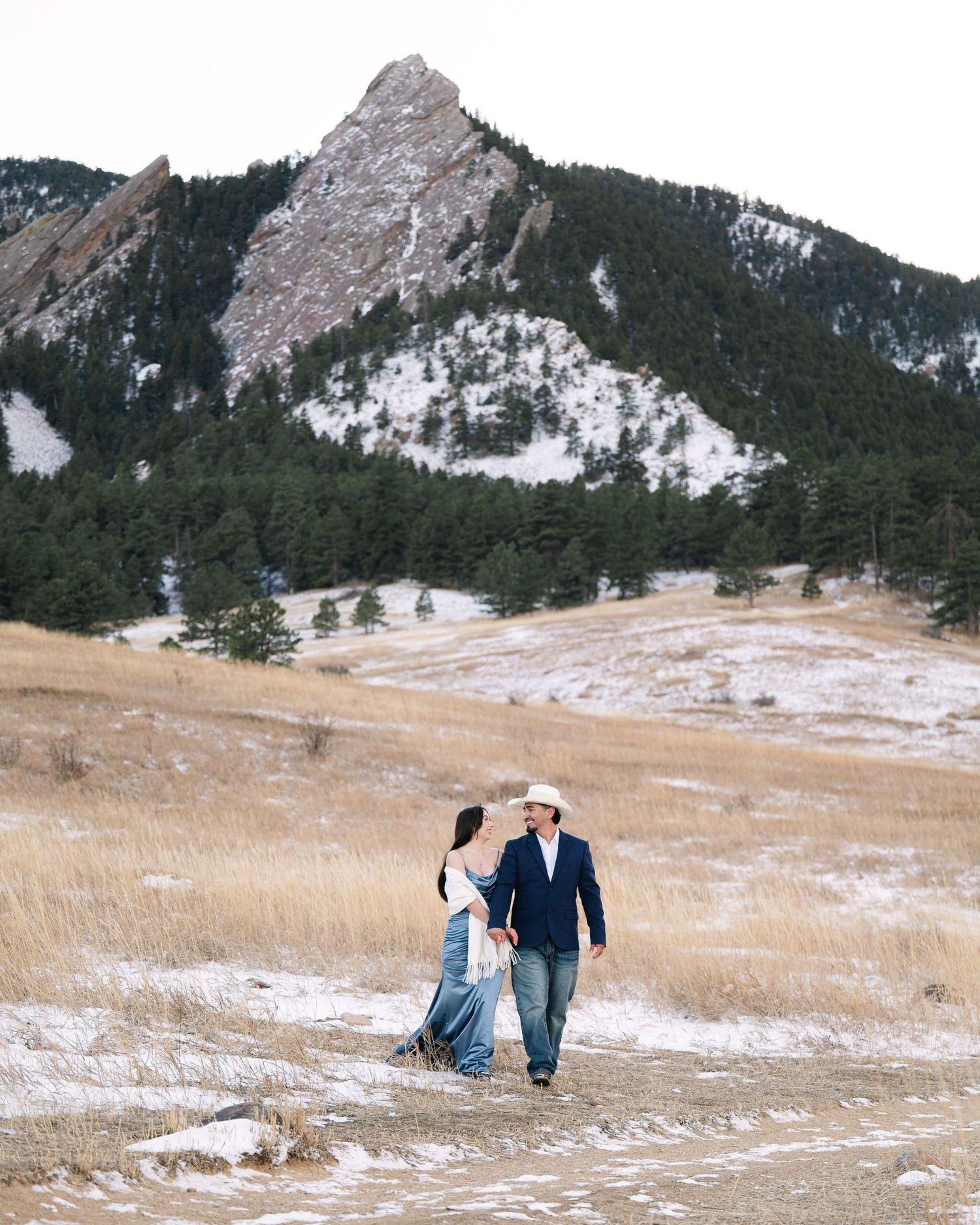 Two people sit on rocky outcrops overlooking a scenic mountain landscape at sunset.