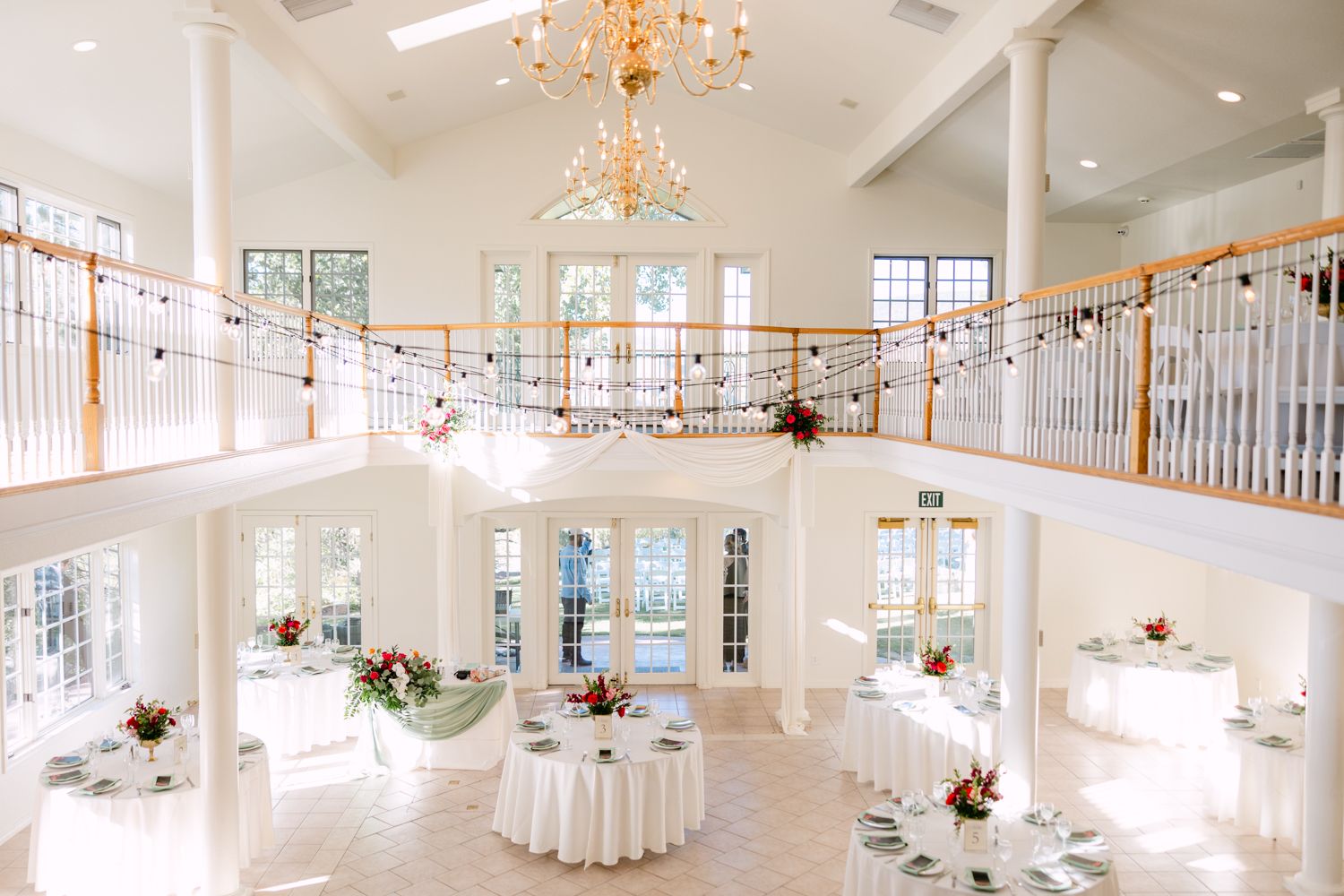 Elegant white wedding venue interior with chandeliers and natural light streaming through large windows.