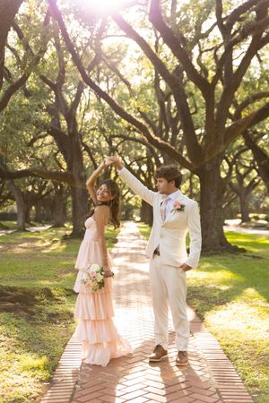 Romantic couple photoshoot on brick pathway under sunlit oak trees.
