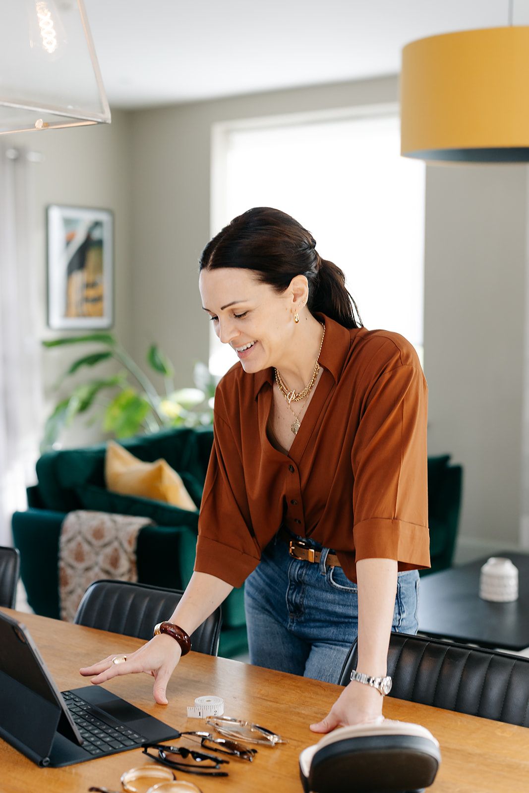 Person in brown shirt working at wooden dining table with laptop and smart speaker in modern home office setting.