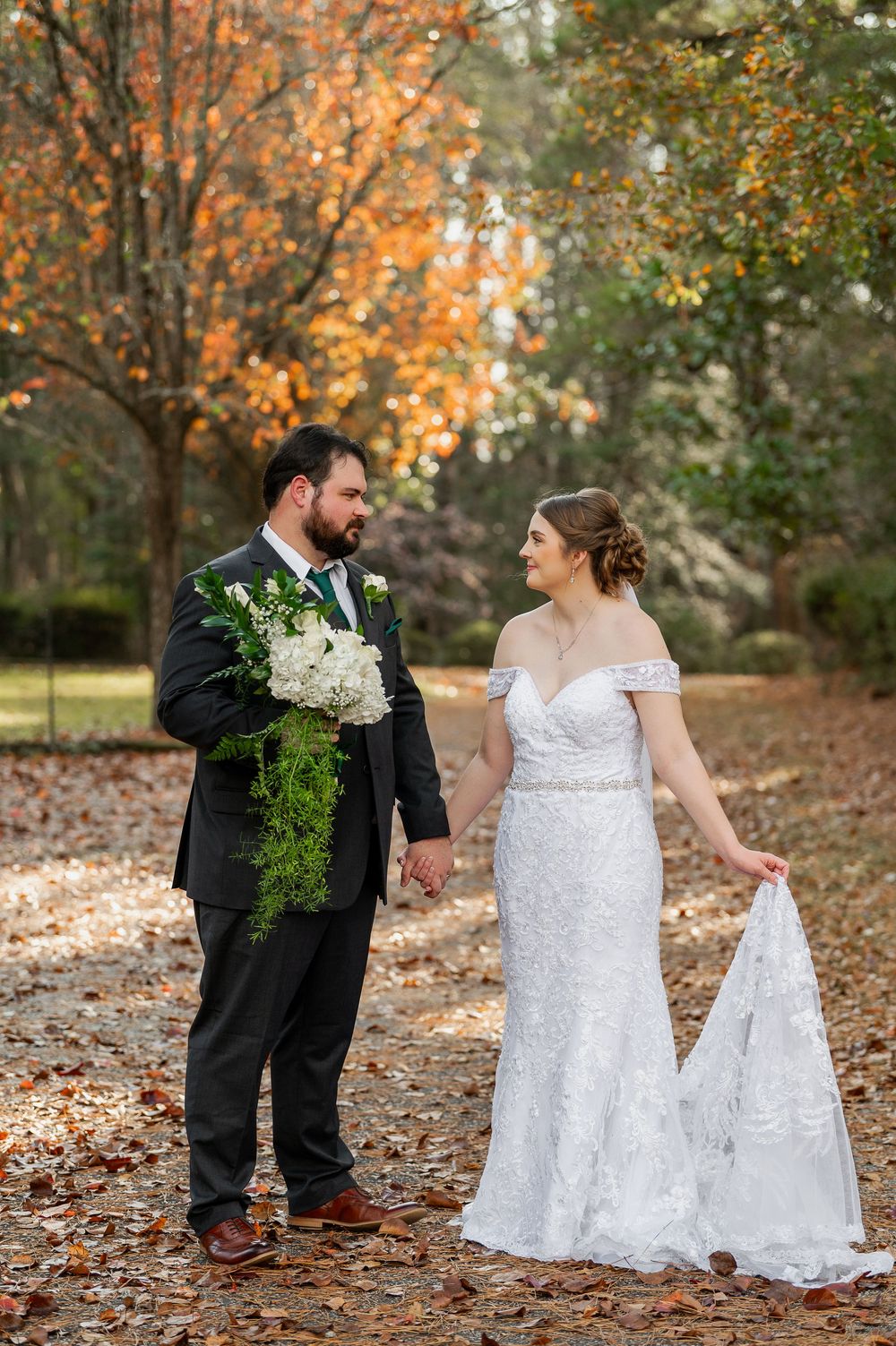 Wedding couple poses playfully among fallen autumn leaves while holding a white bouquet.