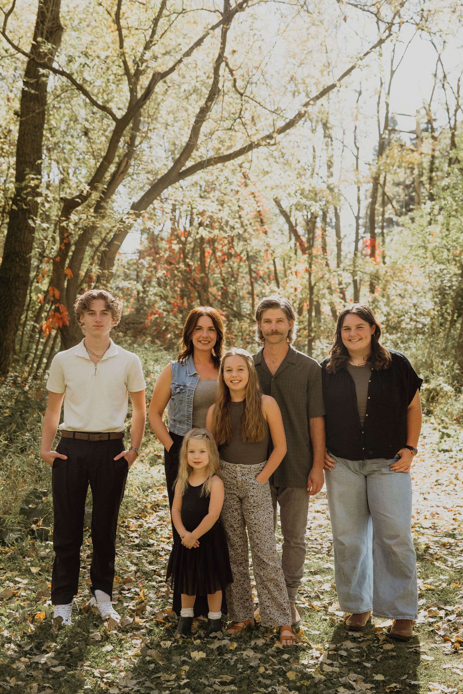 Family of six posing together in a sunlit autumn forest with colorful fall foliage.