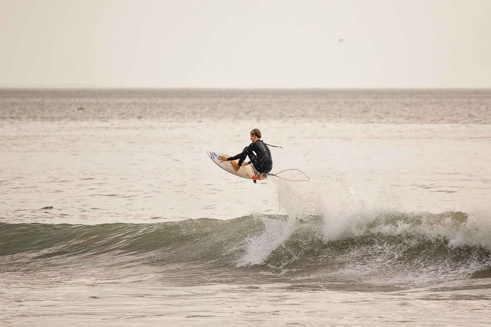 A surfer rides a wave while performing a cutback maneuver, creating a spray of water behind them.