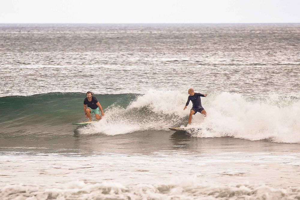 A surfer rides a wave while performing a cutback maneuver on a surfboard during a cloudy day at the beach.