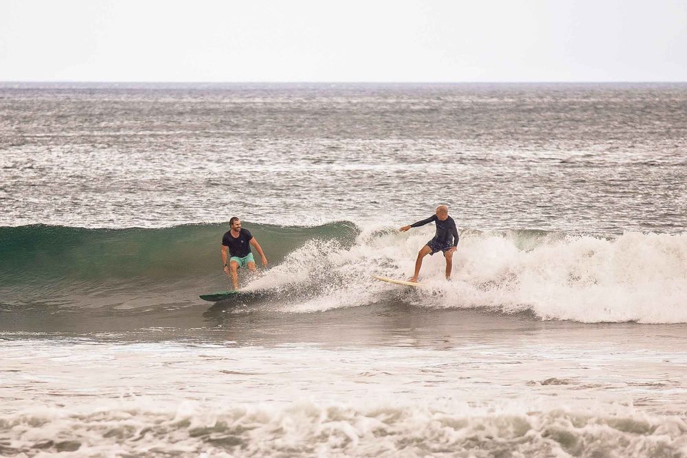 Two surfers ride a turquoise wave together on a misty ocean day.